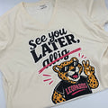 An off-white v-neck tee featuring a graphic of a leopard mascot wearing black sunglasses with 'LEOPARDS' written on it, alongside the text 'SEE YOU LATER, LEOPARDS!' in black and pink lettering.